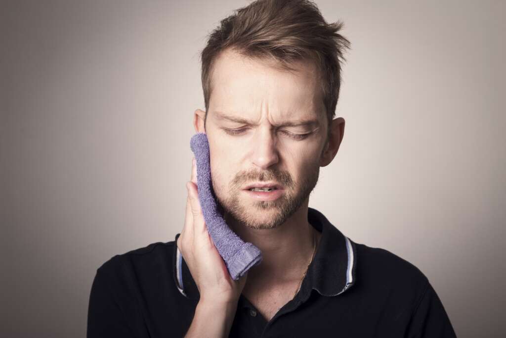 toothache man using a warm cloth to soothe pain in the face